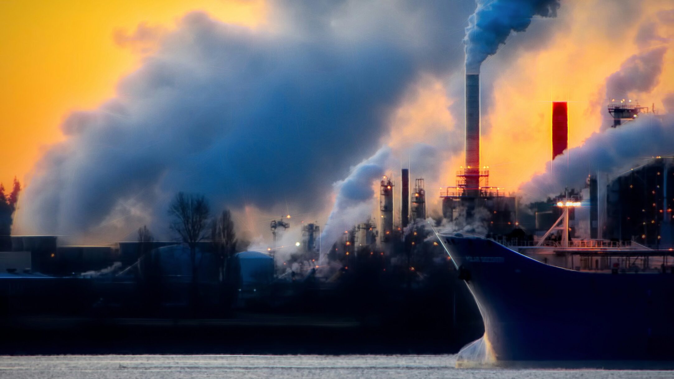 a large boat in a body of water near a factory polluting the environment